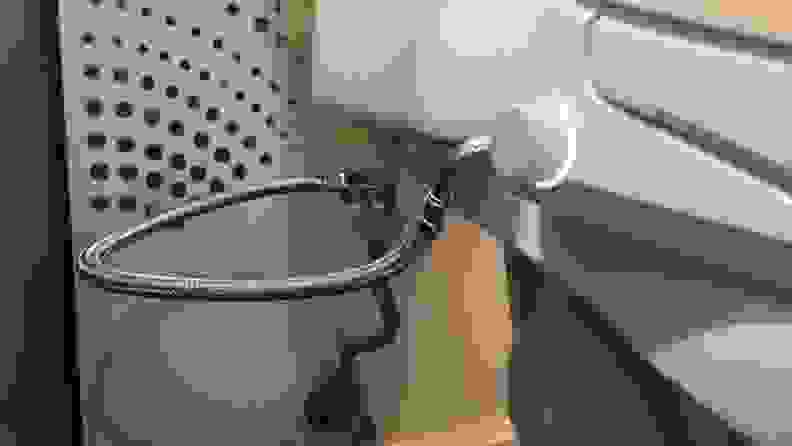 A closeup of the water line connector from the toilet to the bidet, and the control knob with backlight.