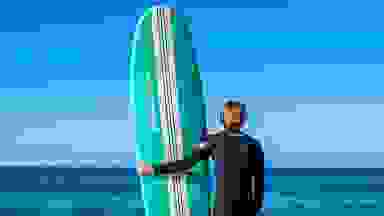 A guy taking his board into the ocean to surf.