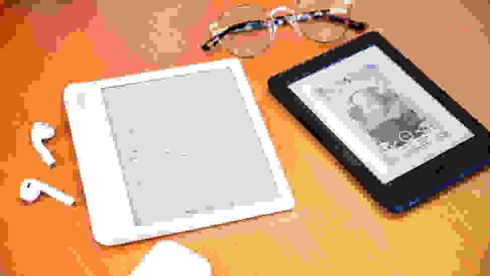 Two e-readers sitting on a wooden surface with a pair of glasses