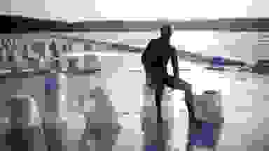A person in a wetsuit sits atop a block of ice on the beach.