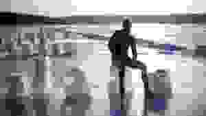 A person in a wetsuit sits atop a block of ice on the beach.