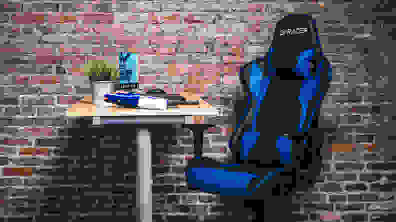 The Homall Gaming Chair, a blue and black gaming chair with racecar seat-like fins, against a brick wall
