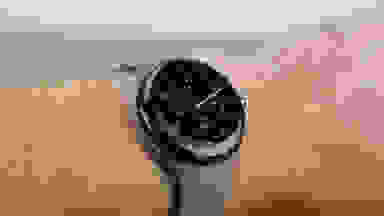 A stylish, round watch sits on a wrist with red digital face and a gray band.
