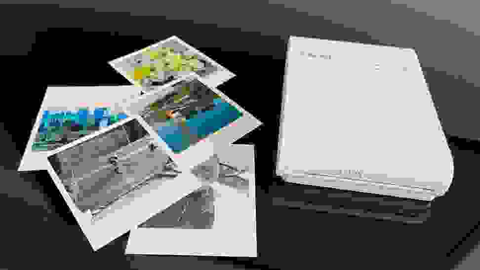 The Canon Selphy portable photo printer on a table next to some photographs.