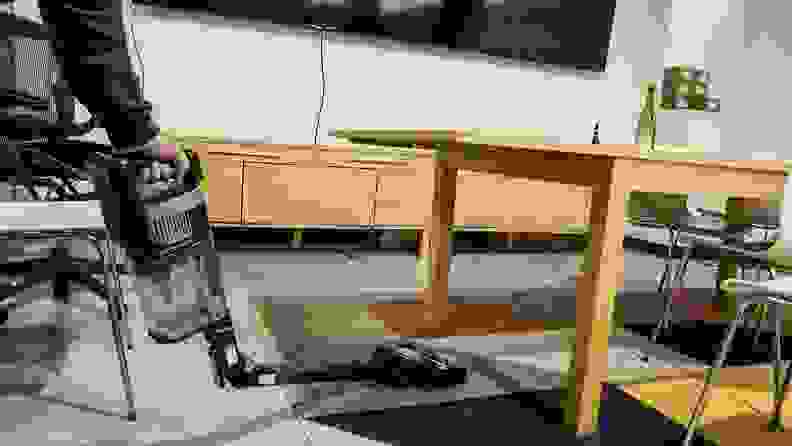 The Shark Stratos cordless vacuum squeezes under a wooden table to clean the floor beneath it.