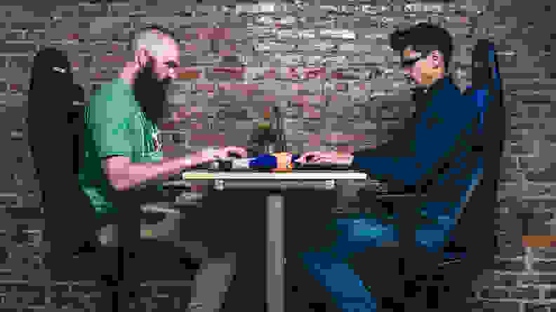 Two testers sitting opposite each other in some of the best gaming chairs on the market right now, against a brick wall