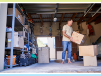 Person standing in garage while holding moving boxes indoors.