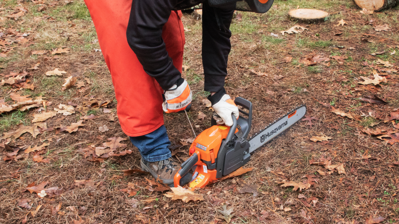 A person outdoors wearing safety gloves while holding a Husqvarna chainsaw