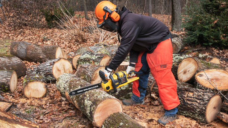 A man uses a Dewalt chainsaw to cut through a large log.