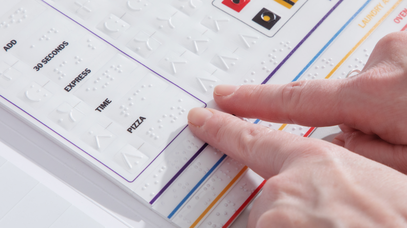 A pair of hands feels along the braille labels for oven functions